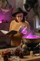 realistic witch brewing potion in cauldron. learns witchcraft from a book. Everyday life intertwined with traditional witchcraft, magic and mystical atmosphere. © Andrii Lysenko