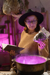 realistic witch brewing potion in cauldron. learns witchcraft from a book. Everyday life intertwined with traditional witchcraft, magic and mystical atmosphere. © Andrii Lysenko