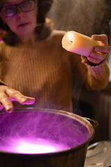 realistic witch with candle over cauldron brewing potion casting spells. Everyday life intertwined with traditional witchcraft, magic and mystical atmosphere. copy space. Halloween horror. © Andrii Lysenko