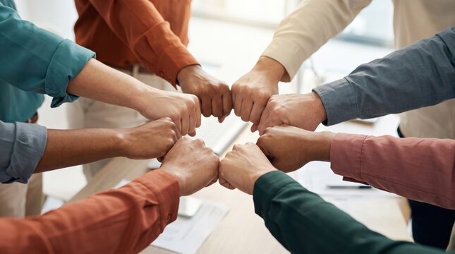 Diverse group of people showing unity and teamwork with a fist bump gesture in a bright, collaborative setting.