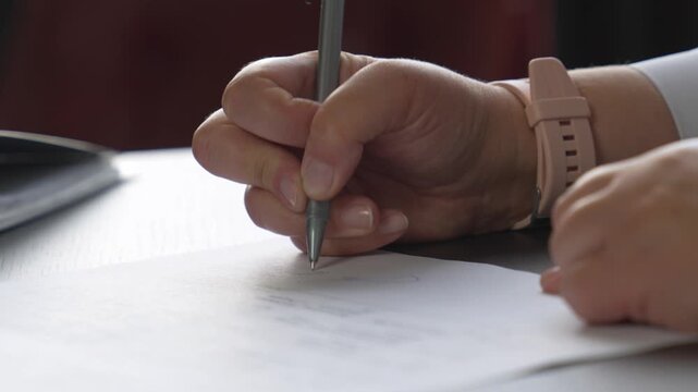 A close‑up of a woman&rsquo;s hand signing with a pen. A woman&rsquo;s hand writing on paper.