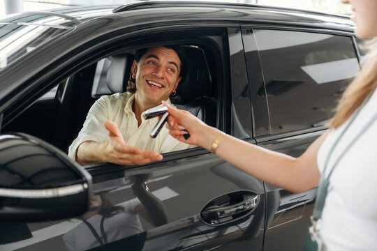 Man receiving car keys from a female salesperson inside a modern automotive dealership, showcasing a sleek black vehicle in the background