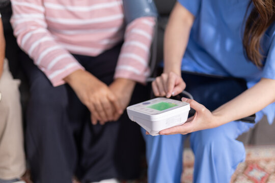 Caring professional nurse checking blood pressure of calm senior patient using digital monitor during routine medical healthcare visit