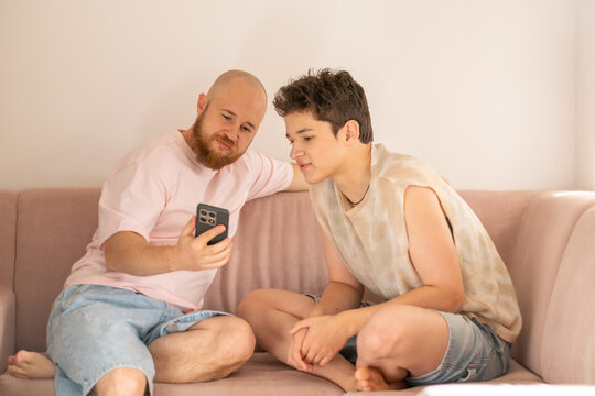 Father shows something on phone screen to his teenage son, father finding common language with teenager, moment building real trust. Wide shot. Concept of father and teenage son sharing screen