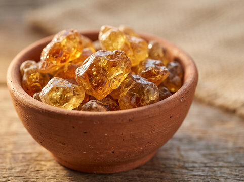 Natural amber gum resins in a terracotta bowl on rustic wooden background, organic edible gum for traditional remedies and culinary use