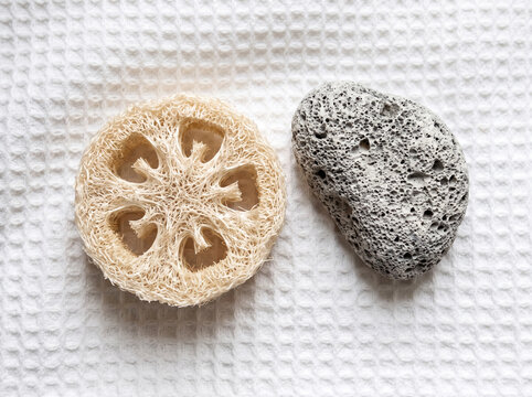Natural loofah sponge and grey pumice stone for body care and exfoliation on a white waffle towel background, top view