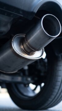 Close-up view of a polished metal car exhaust pipe and muffler system mounted under the rear chassis of a modern vehicle, highlighting automotive performance and mechanical engineering.
