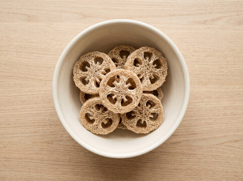 Top view of natural loofah sponge slices neatly arranged inside a white ceramic bowl on a light wooden table background