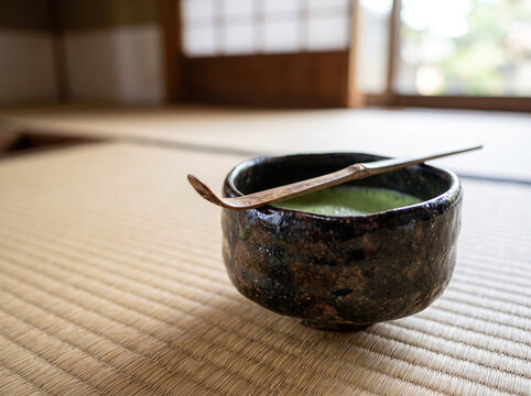 Traditional Japanese matcha green tea in a handmade wabi-sabi ceramic bowl with a bamboo scoop on tatami mats inside a ryokan with shoji screen background.