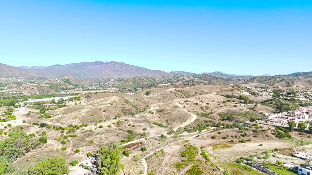 Drone sweeps round to show a beautiful landscape at morning light, with bright blue sky and countryside.