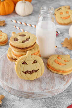 Halloween pumpkin shaped sandwich cookies with sweet cream filling on a wooden board with milk on a concrete background. Jack o lantern cookies