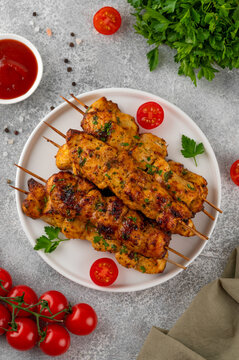 Juicy chicken skewers cooked in an air fryer and served on a plate with fresh herbs, cherry tomatoes and dipping sauce. Healthy food. Top view, copy space.
