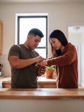 Couple opens stubborn jar lid together in kitchen