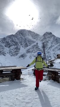 Vertical 4K footage of a snowboarder standing on Mount Cheget summit with the majestic snow-covered peak of Donguzorun mountain and Seven glacier in the background