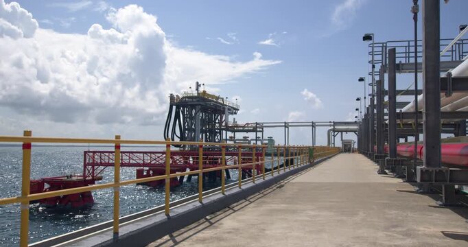 Static wide shot of the pier walkway with yellow safety railings leading toward the offshore loading platform and mooring structure at Coastal Petroleum terminal in San Pedro de Macoris, Dominican Rep