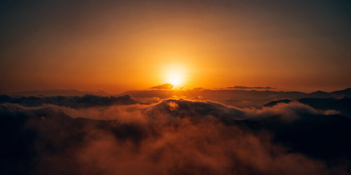 A sunrise over a mountain range with clouds and mist glowing in warm golden light. Dramatic sky and serene landscape, a peaceful and inspiring natural scene