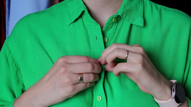 Close-up of hands buttoning a vibrant green linen shirt.
