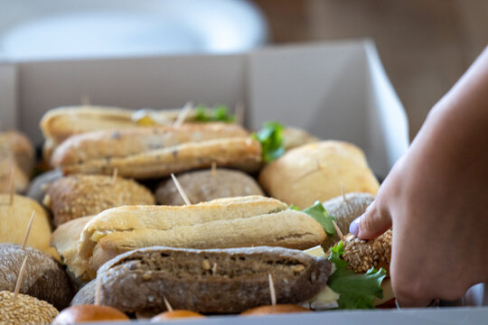Hand Reaching for Fresh Assorted Mini Sandwiches in Catering Box at Wedding Reception