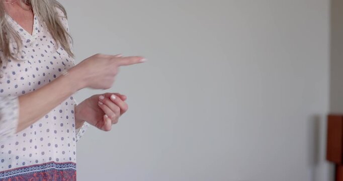 Senior woman gesturing with arm extended at home, wearing polka dot blouse