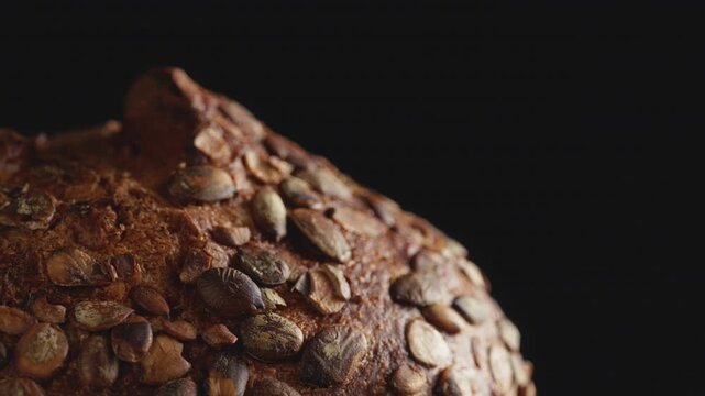 Close-up of artisan whole wheat sourdough bread topped with pumpkin seeds on a dark background. Freshly baked organic loaf with crispy crust for commercial bakery promotions and healthy food concept.