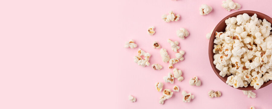 Tasty salty popcorn in a bowl on a pink background