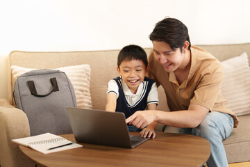 Obraz premium Asian father helping son with laptop homework for back to school education at home