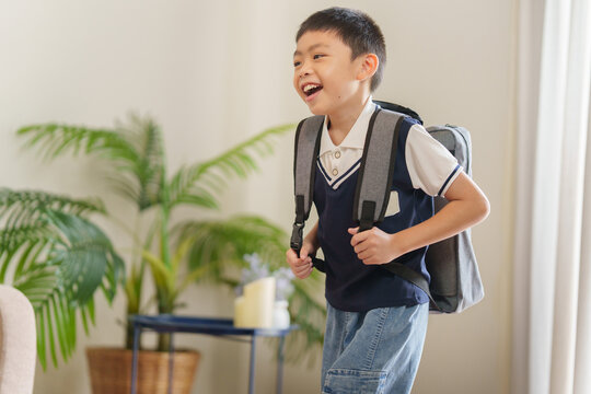 Excited Asian boy carrying backpack ready for back to school season at home