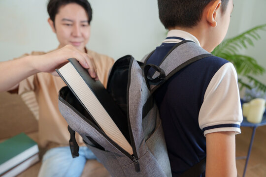 Parent putting textbook into child backpack for back to school preparation