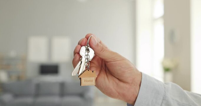 Hand holding house keys symbolizes home ownership. Person presents a keychain with house charm for property sale, mortgage, rental, or relocation. Real estate investment and moving concept.