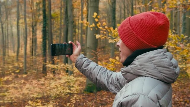 Young man taking pictures with his phone in nature, enjoying the view in a forest in autumn. 