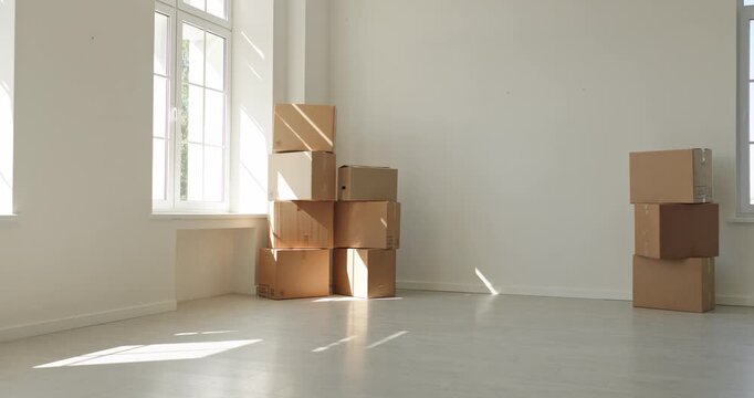 Moving boxes fill an empty apartment with sunlight. Cardboard cartons stand by windows, with space for delivery and packing campaigns. Bright relocation and new home lifestyle concept.