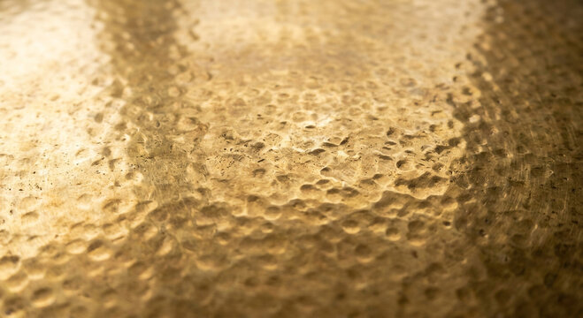 Close up view of a golden hammered metal surface with a rough and uneven textured finish