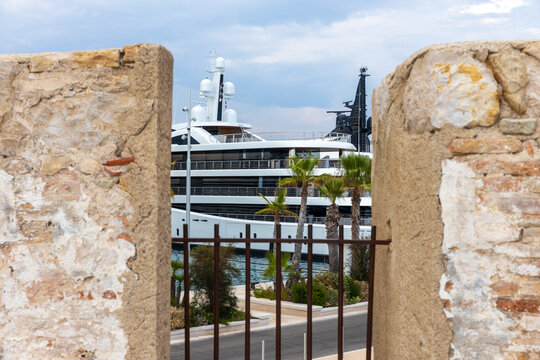 Luxury Superyacht Moored in Mediterranean Marina Framed by Historic Stone Wall and Palm Trees