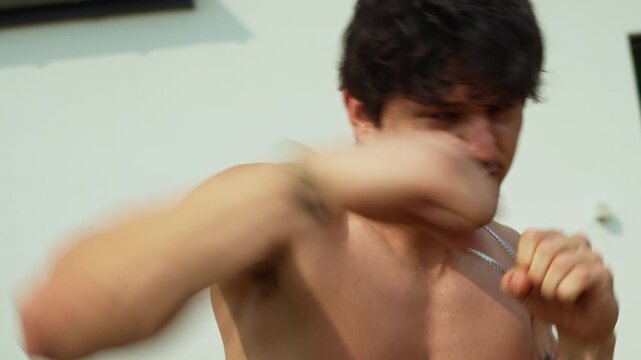 Young hispanic male outdoor shadowboxing during hot summer day. Aggression during throwing combination punches.