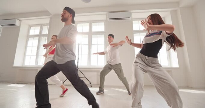Young dancers practice energetic hiphop dance in studio. Friends rehearse synchronized moves in a bright sunlit dance room, wearing activewear. A joyful concept of teamwork and expression.