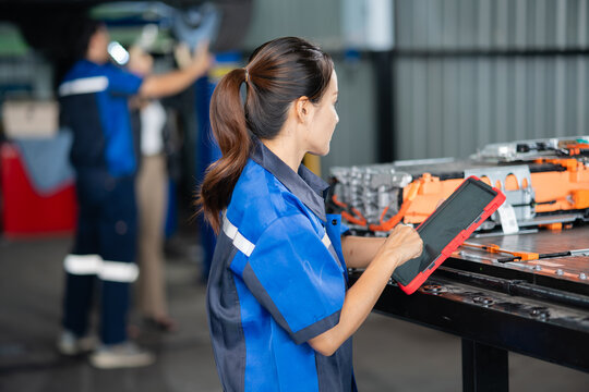 An electric vehicle battery technician uses a tablet beside the open pack while a colleague and the customer inspect the car.