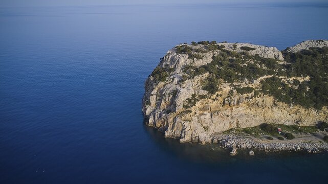 Drone shot, A rocky coastline with a rugged rocky outcrop bordered by calm sea and blue sky, Anthony Quinn Bay, Vagies Bay, Rhodes, Dodecanese, Greek Islands, Greece