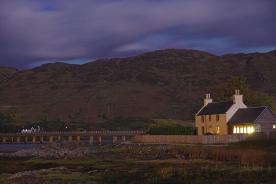 Illuminated house in a remote area against a hilly background at night, Dornie, October, Scotland, United Kingdom