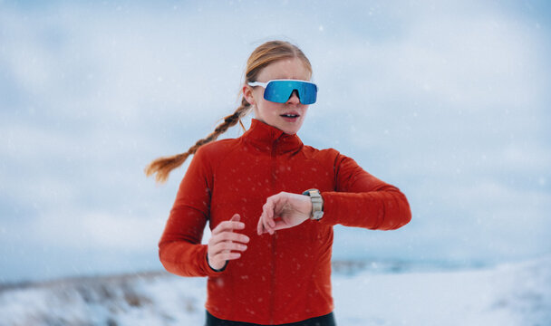 Woman checking smartwatch during winter running training in falling snow