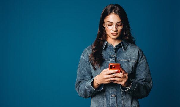 Woman using smartphone for mobile communication in studio against blue background
