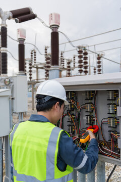 Cabinet inspection in a substation switchyard shows a clamp meter reading being taken on wiring inside an open control cabinet.