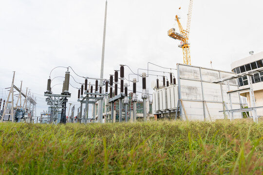 Outdoor high-voltage substation contains a transformer, insulators, and disconnect switches behind a concrete fire wall near a transmission tower.