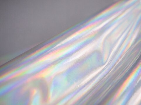 Holographic iridescent foil texture, shimmering rainbow metallic surface, abstract pearlescent chrome background with light refraction and soft folds