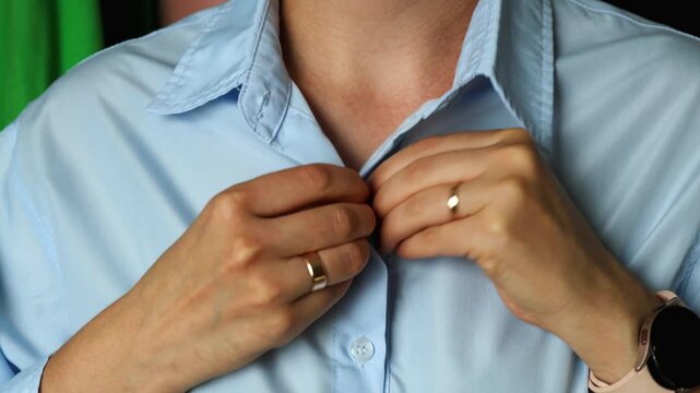 Close-up of a person buttoning a blue cotton shirt.