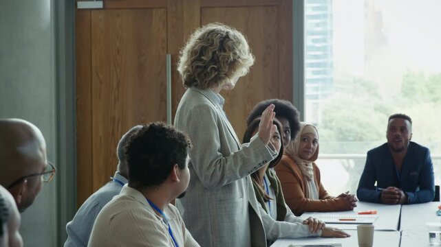 A diverse group of professionals are actively engaged in a business meeting, with one woman presenting and others listening intently. This scene captures teamwork and collaboration.