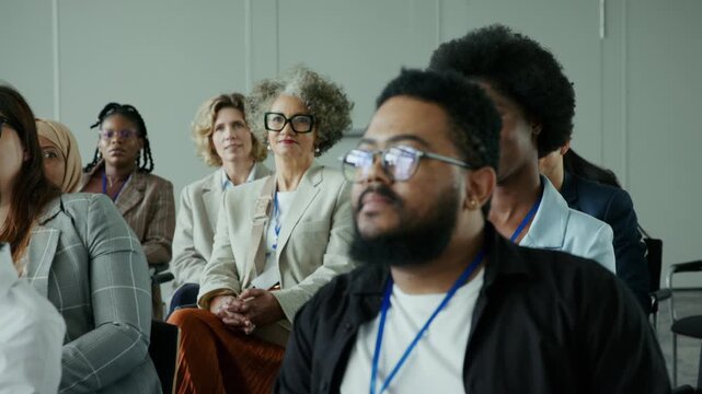 Diverse professionals attend a conference, actively listening and engaging. The audience represents various backgrounds, contributing to a dynamic learning environment. One person prepares to speak.