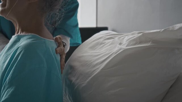 Nurse fluffing pillow and helping senior Caucasian woman rest comfortably in hospital bed. Clip suitable for advertising geriatric healthcare services, elderly nursing care, and hospice support