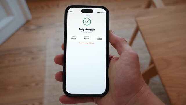 A confirmation reports that the electric car is fully charged and ready for the range ahead. Point of view shot with the phone held in the hand. Useful for electric mobility marketing.