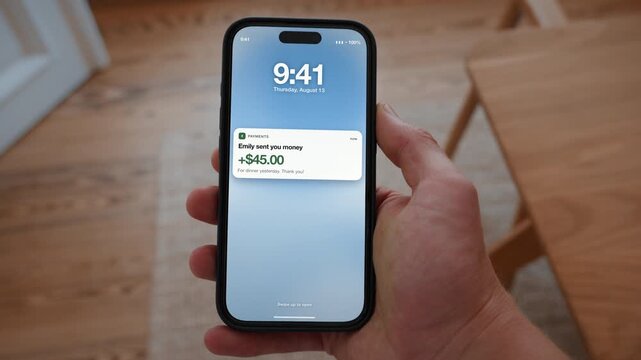 A peer to peer payment arrives and the amount appears as a notification on the phone. Point of view shot with the phone held in the hand. Useful for sharing costs among friends.