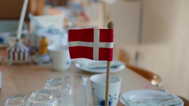 A tiny Danish flag stands on a table set for a family birthday at home, evoking Nordic tradition, hygge and shared celebration moments.